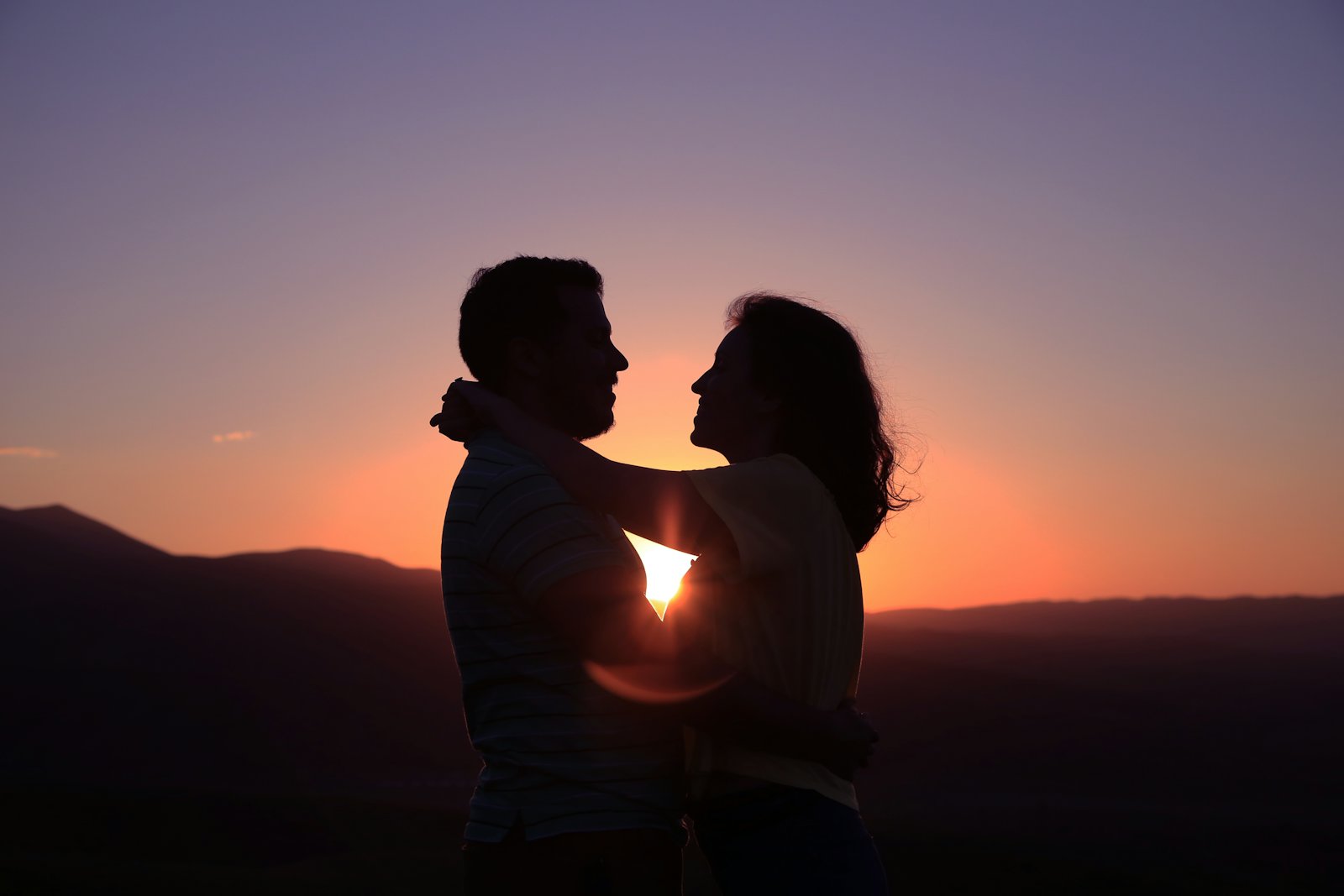 Couple silhouetted against a sunset over the ocean