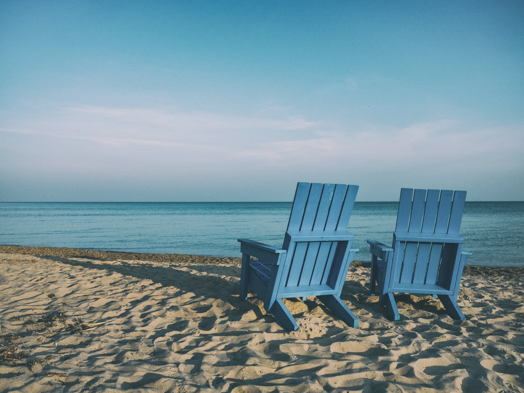 Two blue chairs on a sandy beach